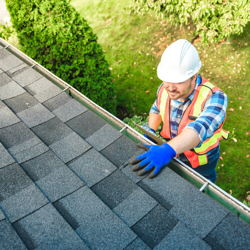 A man with hard hat standing on steps inspecting house roof